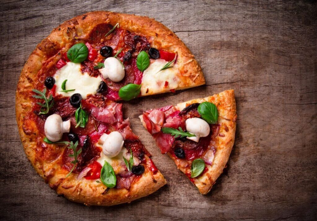 A pizza cut in half on top of a wooden table.